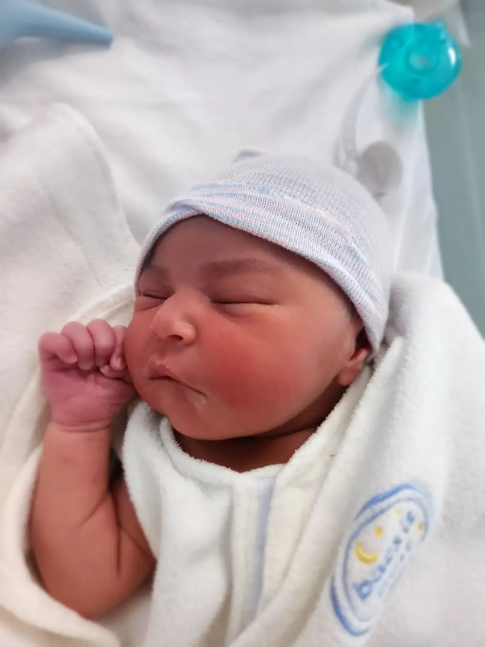 A newborn sleeping wrapped in a blanket, wearing the hospital cap